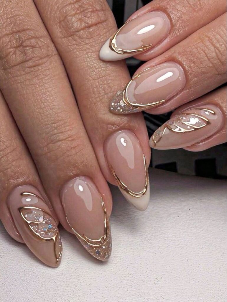 Glossy nude almond press-on nails with gold outline French tips and subtle glitter accents.